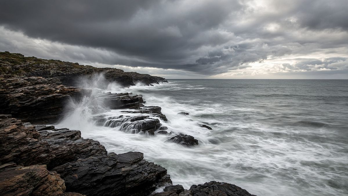 Waves crashing on a rugged rocky coast under storm clouds